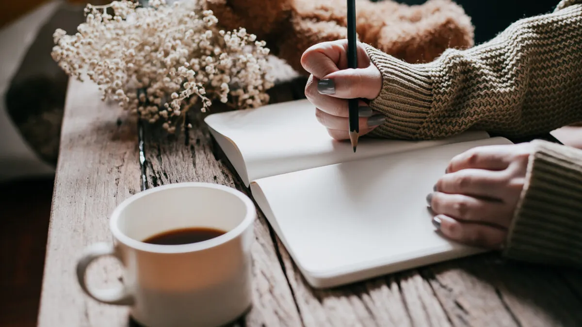 Person journaling with coffee tracking daily energy patterns
